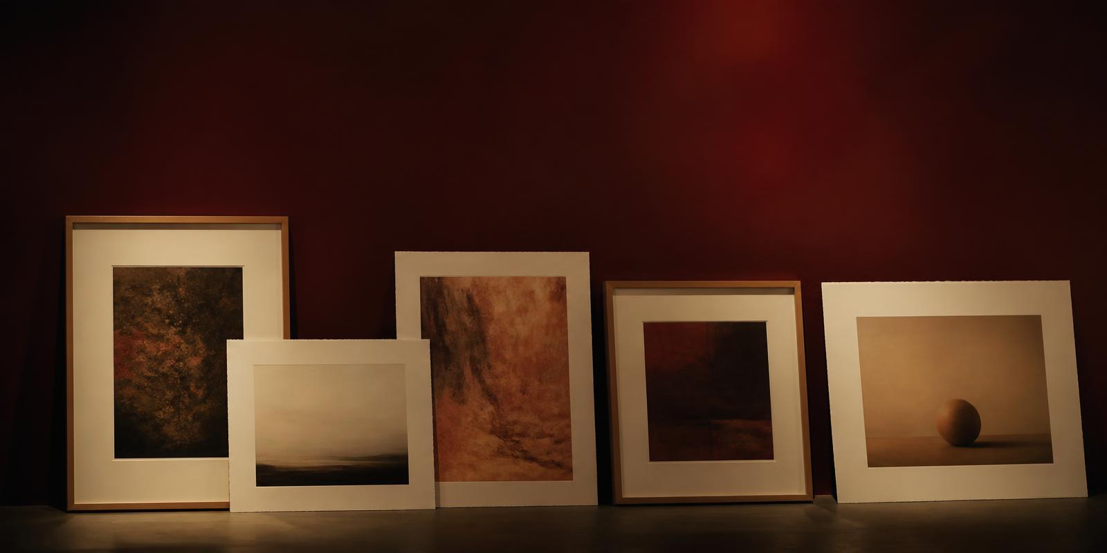 Framed and unframed archival prints leaning against a deep burgundy gallery wall