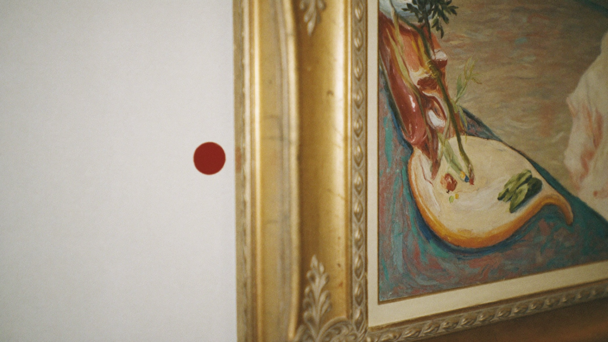 A red sold dot beside a gold picture frame on a gallery wall