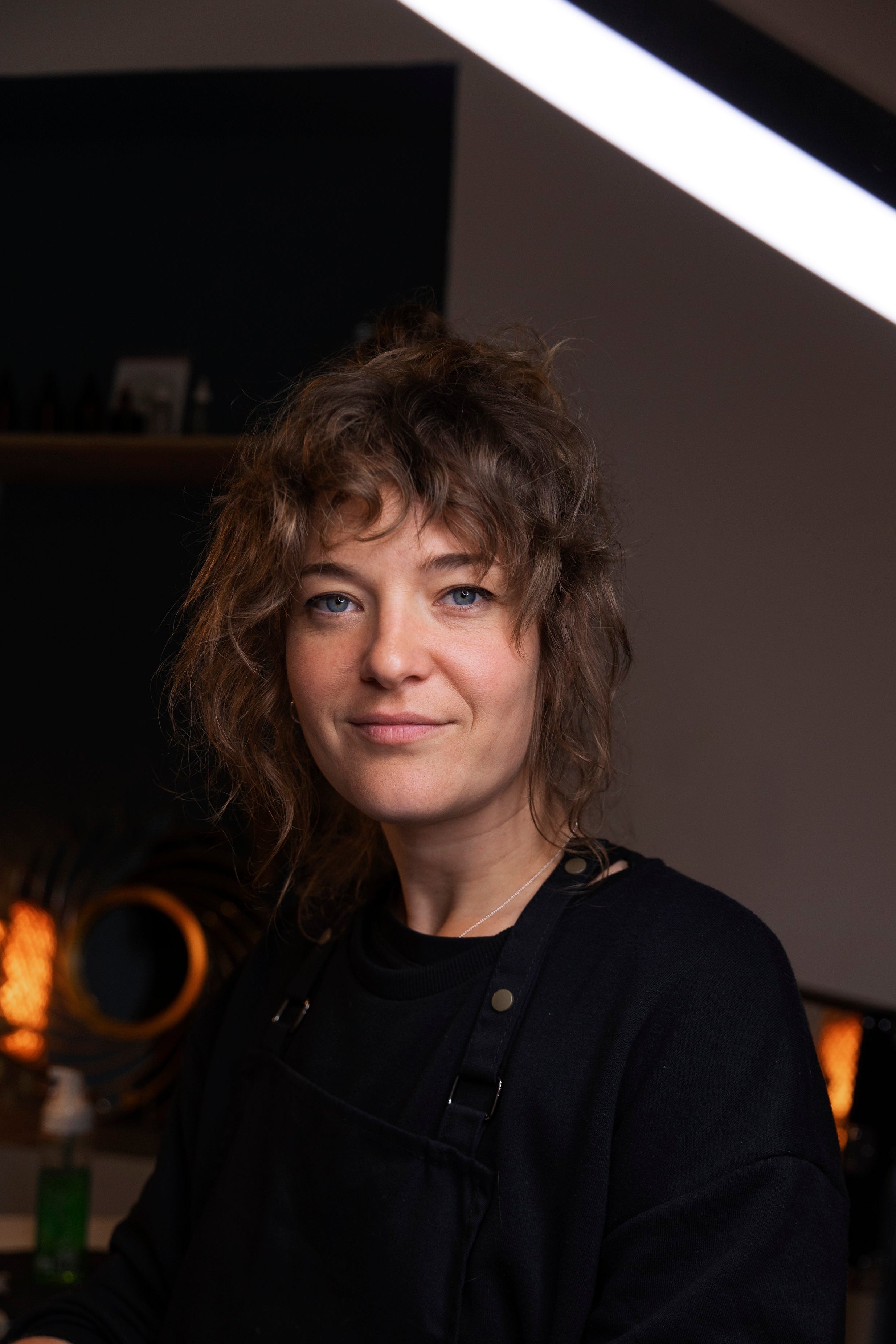 Person with shoulder-length hair wearing a black shirt in a dimly lit room.