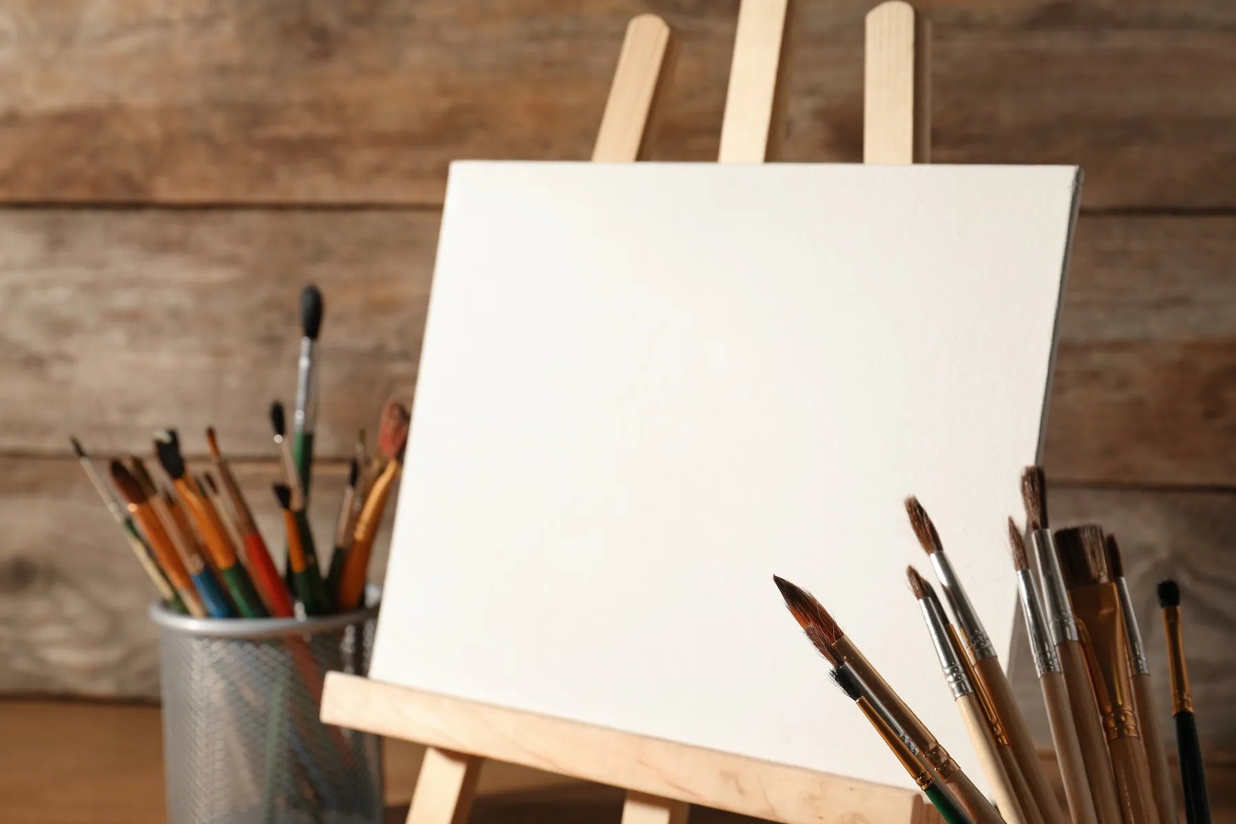 Easel with a blank canvas and paintbrushes on a wooden background